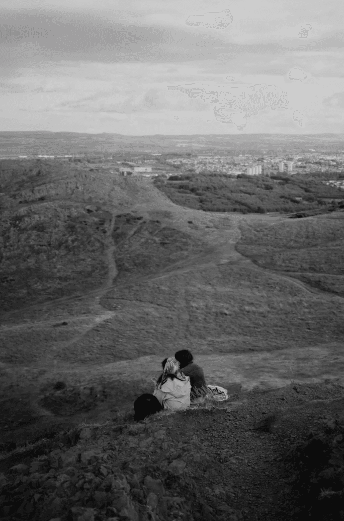 Un couple assis en haut d'une colline, regardant le paysage ensemble.